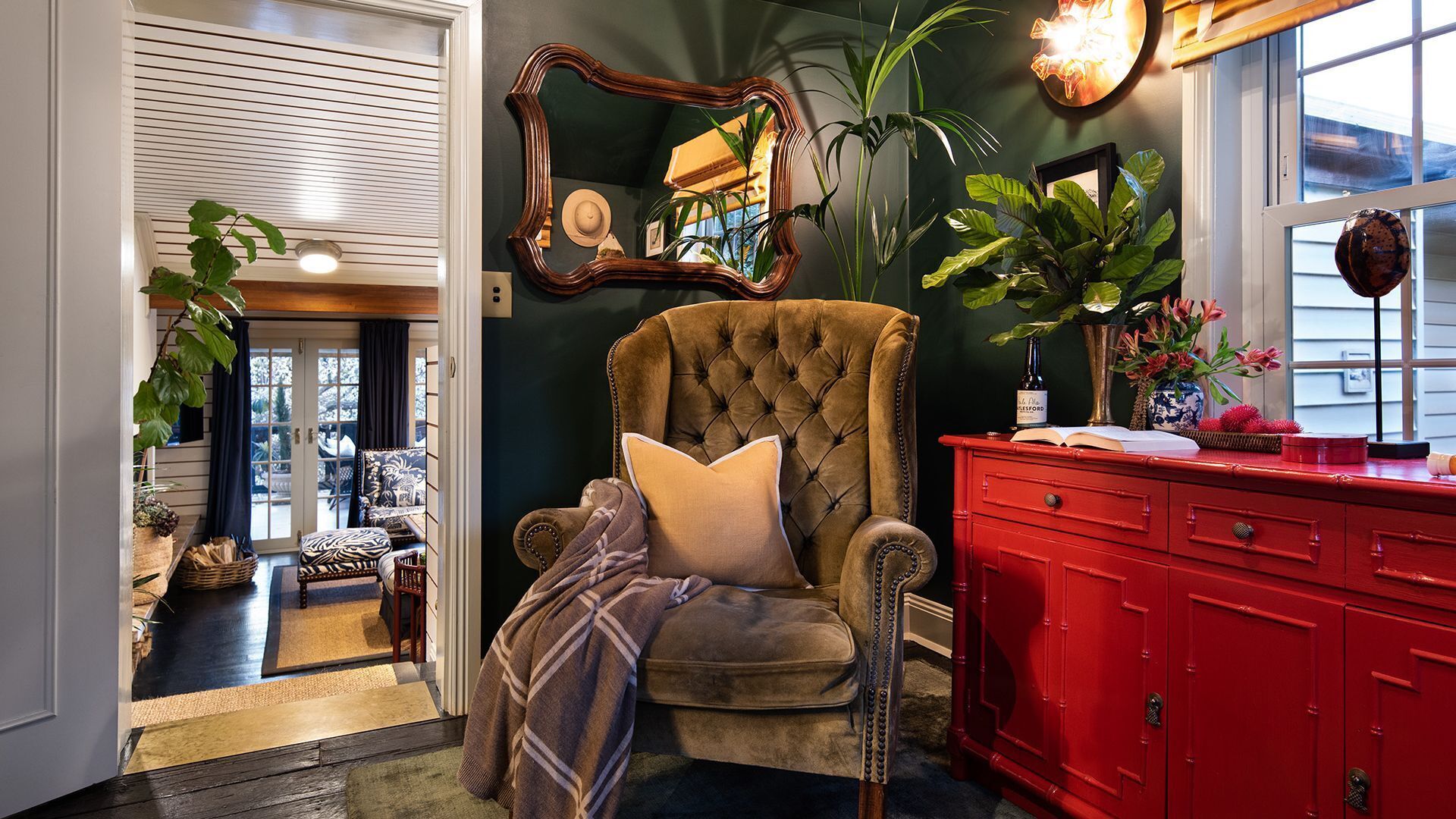 A room with a tufted armchair, a red dresser, and a mirror on the wall.