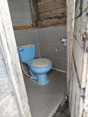 A small, enclosed bathroom with a blue toilet, a wooden floor, and a tiled wall. - Eco Office for Digital Nomads | Solar + Starlink + Views (Puntarenas)
