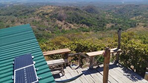 Terraço com painéis solares, mesas de madeira e vista para uma paisagem montanhosa.