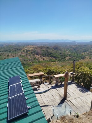 Eine Dachterrasse mit Solaranlagen, Holztischen und Blick auf eine hügelige Landschaft.