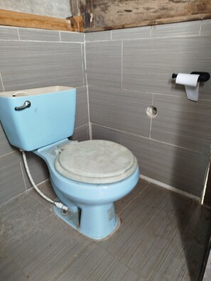 A bathroom with a blue toilet, grey tiled walls, and a wooden beam above. - Eco Office for Digital Nomads | Solar + Starlink + Views (Puntarenas)