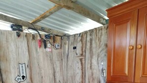 Um quarto pequeno e rústico, com uma cama de solteiro, um armário de madeira e diversos tomadas na parede.