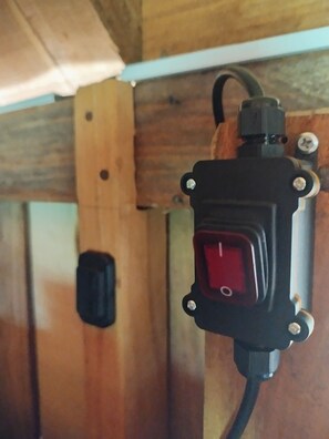 A power outlet with a red switch, a black plug, and a white cable. - Eco Office for Digital Nomads | Solar + Starlink + Views (Puntarenas)