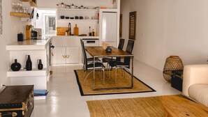 A modern kitchen with white cabinets, a dining area with a wooden table and chairs, and a hanging light fixture. - Casa Pura Vida By Gt House (Reguengos de Monsaraz)