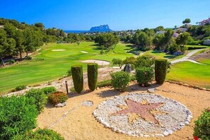 Ein Golfplatz mit einem sternförmigen Bunker, ordentlich geschnittenen Hecken und einer entfernten Bergblick.