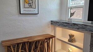 A modern kitchen with a wooden console table, a white wall with a framed artwork, and a window with a view of a building. - Central Close to Downtown, Airport, Fort bliss, Restaurants , Entertainment,UTEP (El Paso)
