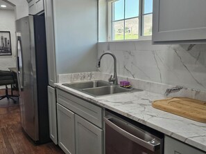 Una cocina con un refrigerador de acero inoxidable, un lavamanos doble y una tabla de cortar de madera.