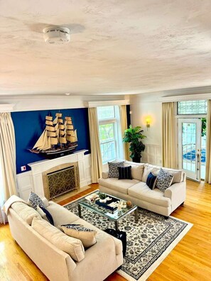 Ein Wohnzimmer mit Kamin, zwei Sofas, einem Couchtisch und einem großen Gemälde eines Schiffes an der Wand.