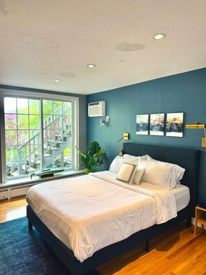 Ein Schlafzimmer mit einem großen Bett, einem Fenster mit Blick auf Treppen und Grünflächen sowie einer Wand-Klimaanlage.