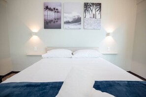 Une chambre d’hôtel avec un lit, deux lampes fixées au mur et trois tableaux encadrés accrochés au mur.