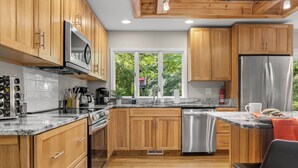 Cozinha moderna com armários de madeira, eletrodomésticos de aço inoxidável e uma janela com vista para o verde lá fora.