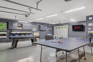 Une pièce équipée d’une table de billard, d’une table de ping-pong et d’un téléviseur sur lequel est affiché le logo « NETFLIX ».