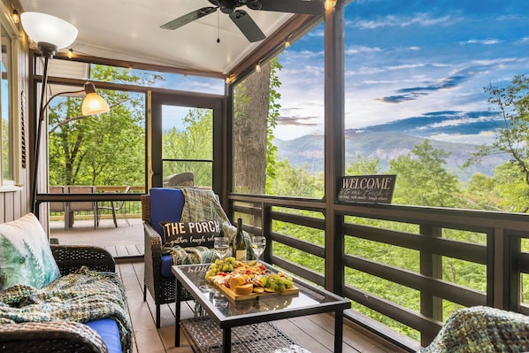 Une véranda abritée avec une table dressée pour un repas, une chaise en osier et une vue sur les montagnes.