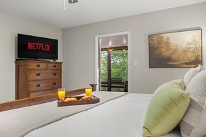 Makuuhuoneessa on sänky, televisio, jossa näkyy Netflix, puinen lipasto, tarjotinalus aamiaistarvikkeineen ja ikkuna, jossa on kyltti, jossa lukee ”TERVETULOA”.