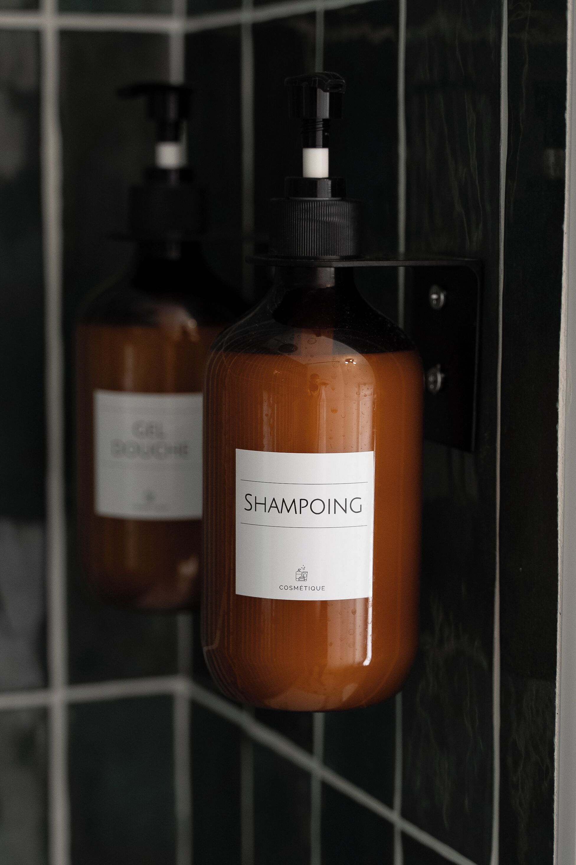 Two bottles of shampoo hanging on a tiled wall.