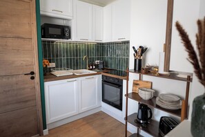 Une cuisine avec des meubles blancs, un four à micro-ondes, un four traditionnel, un évier et une machine à café.