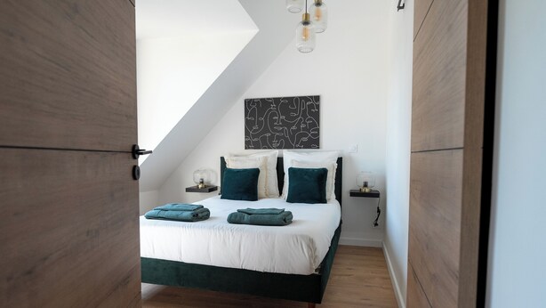 Quarto com cama, piso de madeira, pintura abstrata em preto e branco e luminária no teto.