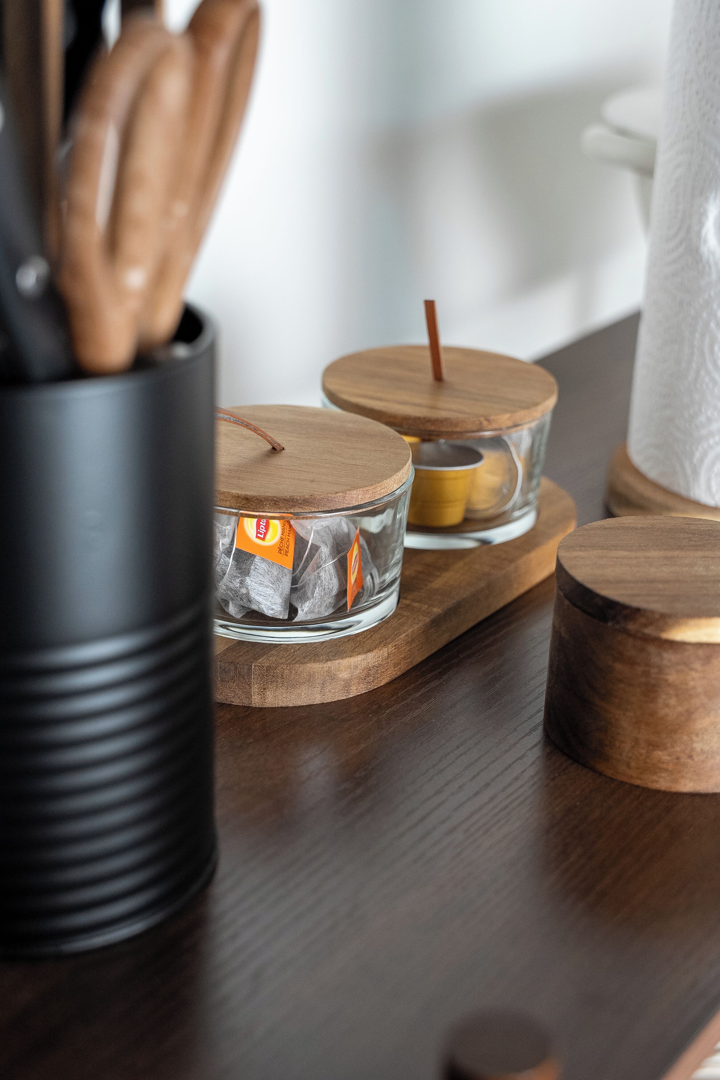 Ein Holztisch mit einer schwarzen Box, Glasbehältern mit Deckeln und einem Kerzenhalter.