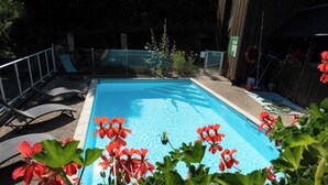 Piscina com superfície de água azul translúcida, cercada por uma grade de metal, e flores vermelhas em primeiro plano.