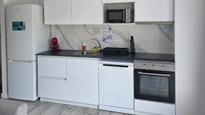 Ett kompakt kök med vita skåp, en inbyggd mikrovågsugn, en diskmaskin och en ugn.