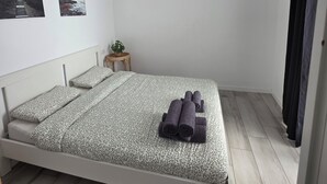 Ett minimalistiskt sovrum med en säng, ett litet sängbord, en väggmonterad luftkonditioneringsanläggning och två inramade tavlor.