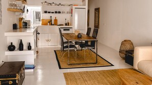 A modern kitchen with white cabinets, a dining area with a wooden table and chairs, and a hanging light fixture. - Casa Pura Vida By Gt House (Reguengos de Monsaraz)