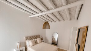 A bedroom with a bed, nightstand, mirror, and a ceiling with exposed beams. - Casa Pura Vida By Gt House (Reguengos de Monsaraz)