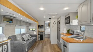 Interior compacto de uma van, com cozinha compacta, sofá cinza e teto de madeira.
