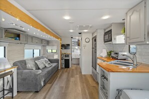 A compact RV interior with a kitchenette, a gray sofa, and a wooden ceiling. - New Tiny Home + Camper - Sleeps up to 10 - Fire Pits - Access to Brimstone Trail (Huntsville)