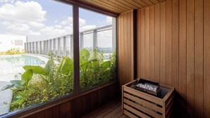 Quarto com teto de madeira, grandes janelas com vista para uma piscina e vegetação, e um caixote de madeira com objetos.