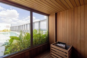 Ein Zimmer mit Holzboden, großen Fenstern mit Blick auf einen Swimmingpool und Grünflächen, sowie einer Holzkiste mit Gegenständen.