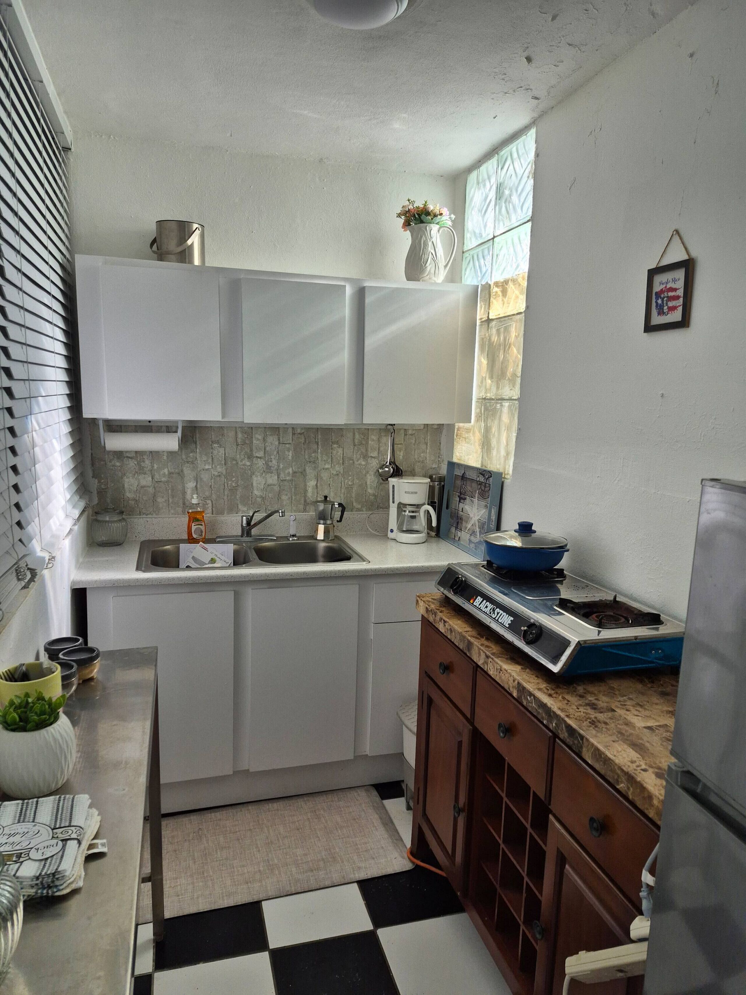 A compact kitchen with white cabinets, a coffee maker, a stove, and a sink.