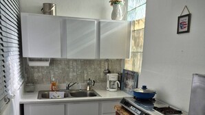 Una cucina compatta con mobili bianchi, una macchina da caffè, un fornello e un lavandino.