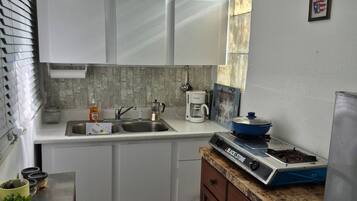 A compact kitchen with white cabinets, a coffee maker, a stove, and a sink.