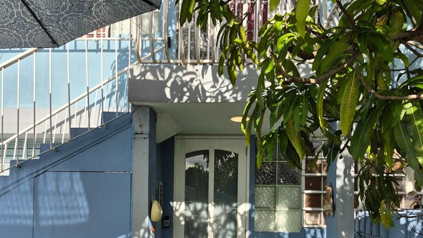 Un edificio blu con porta in vetro, una scala e un piccolo giardino con erba sintetica e sedie in metallo.