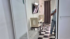 Una stanza con pavimento a scacchi, un divano, un televisore montato a parete e uno specchio che riflette una parte della stanza.