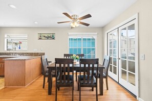A dining area with a wooden table, chairs, a ceiling fan, and a view through large glass doors. - Mission Beach Gem | Patio, Garage & Balcony (San Diego)