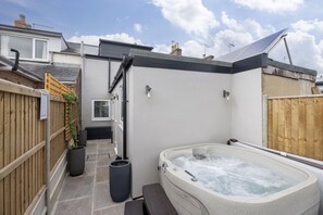 A hot tub in a backyard with a wooden fence, potted plants, and a clear sky. - Stylish Two-Bed Cheltenham Retreat with Hot Tub (Cheltenham)