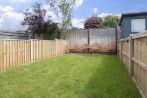 A backyard with a wooden fence, a grassy lawn, and four wicker chairs. - Stylish Two-Bed Cheltenham Retreat with Hot Tub (Cheltenham)