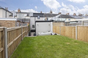 Un patio trasero residencial con un jacuzzi, cerca de madera y casas al fondo.