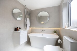 A modern bathroom with a freestanding bathtub, a toilet, and two wall-mounted mirrors. - Stylish Two-Bed Cheltenham Retreat with Hot Tub (Cheltenham)