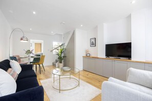 Una sala de estar moderna con un sofá, una mesa de centro de vidrio, un televisor y un área de comedor con una mesa y sillas.