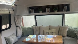 A cozy RV interior with a wooden table, cushioned seating, and a window with curtains.
