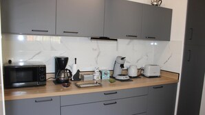 A kitchen with grey cabinets, a microwave, a coffee maker, a toaster, and a kettle. - Thieman House - MENTON (MENTON)