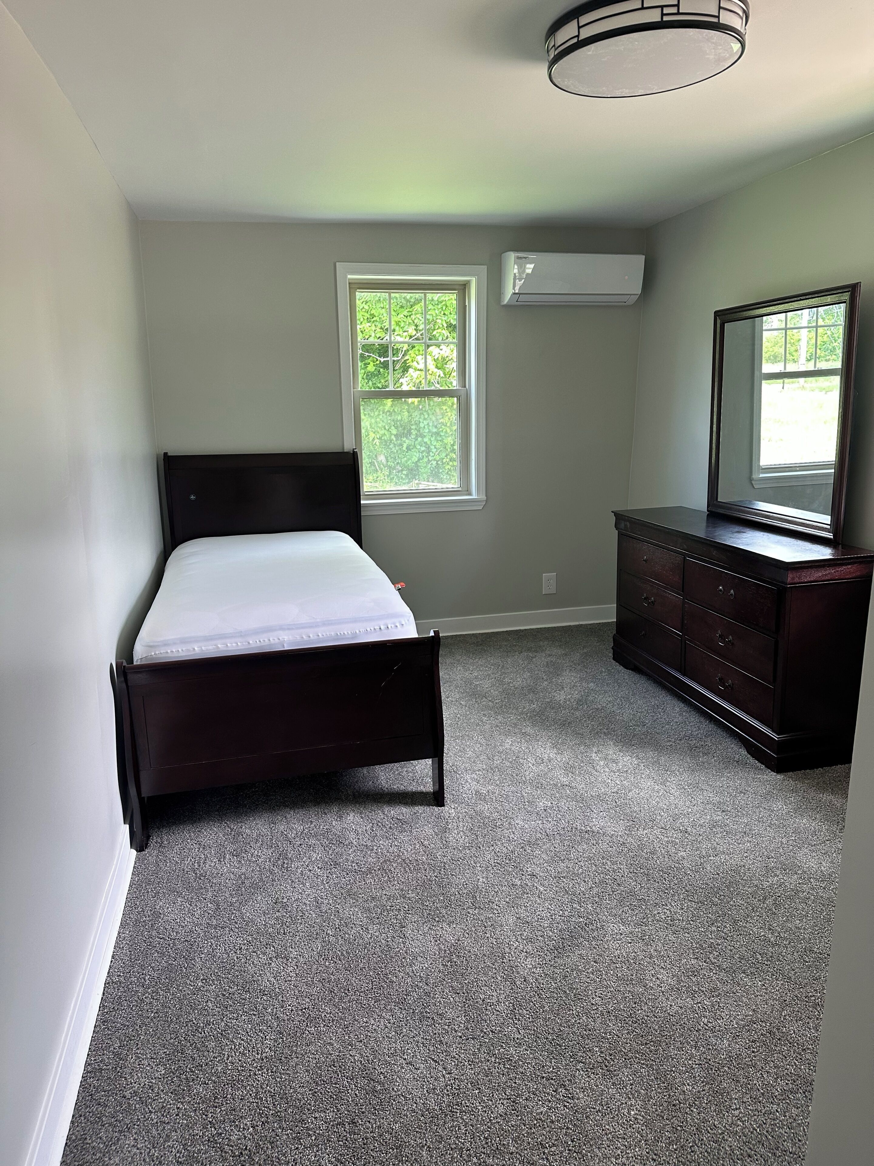 Een slaapkamer met een bed, dressoir, raam en airconditioning.