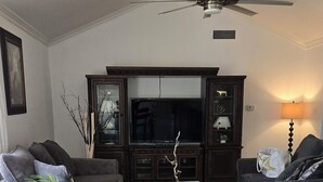 Ein Wohnzimmer mit Deckenventilator, dunklen Holzschränken, einem Flachbildfernseher und zwei Sofas.