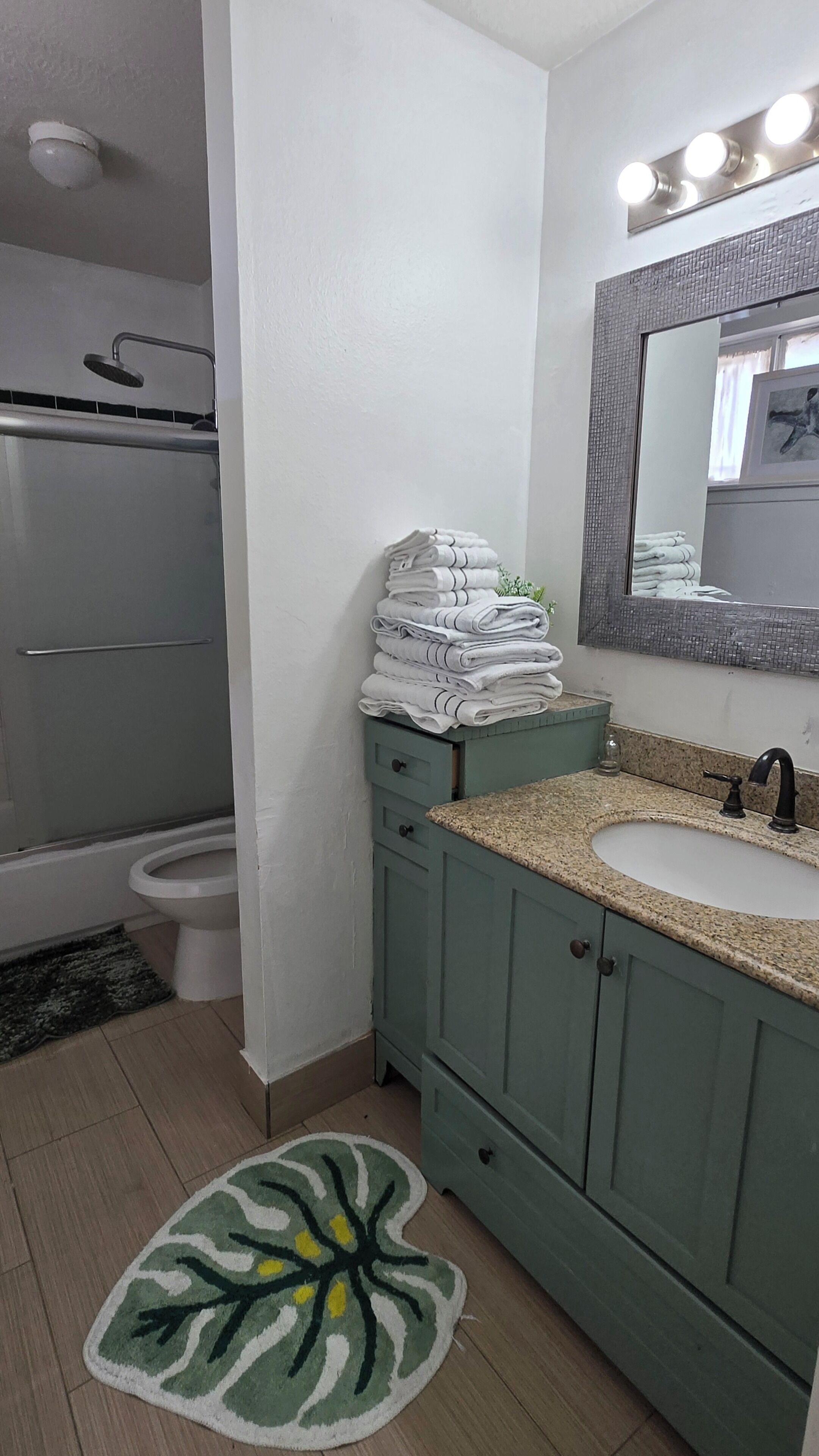 A bathroom with a shower, toilet, sink, and a mirror with lights.