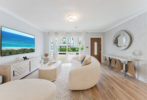 Un salon moderne doté d’un grand téléviseur à écran plat, d’un canapé, d’une table basse et d’un coin repas avec un banc.