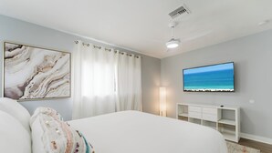 Ein Schlafzimmer mit einem Bett, einem Fernsehgerät an der Wand, einem Deckenventilator und einem Gemälde.