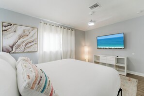 Ein Schlafzimmer mit einem Bett, einem Fernsehgerät an der Wand, einem Deckenventilator und einem Gemälde.